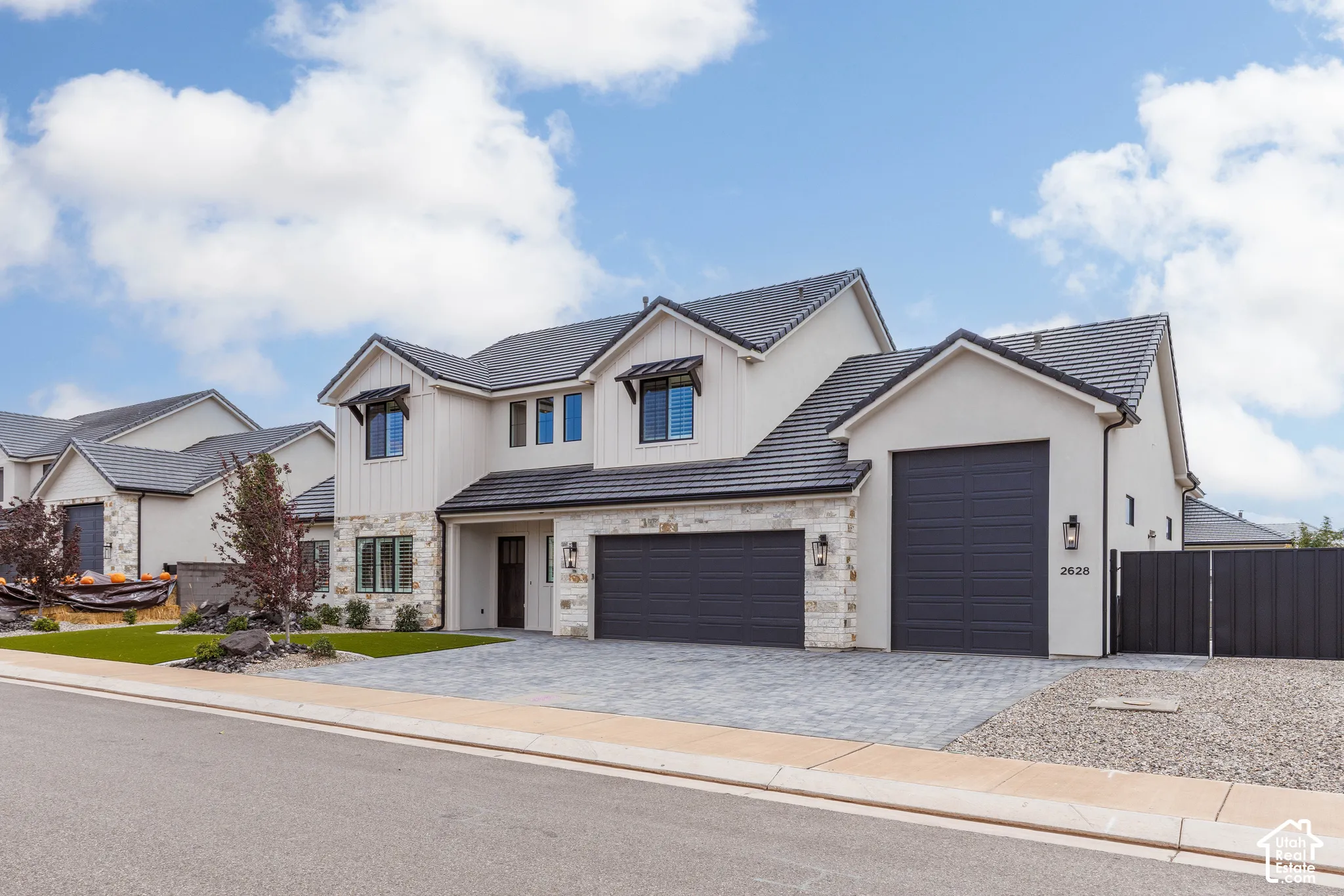 Two-story exterior featuring light-toned masonry accents, vertical siding, multi-car garage with dark-finish doors, dark tile roof, and paved driveway