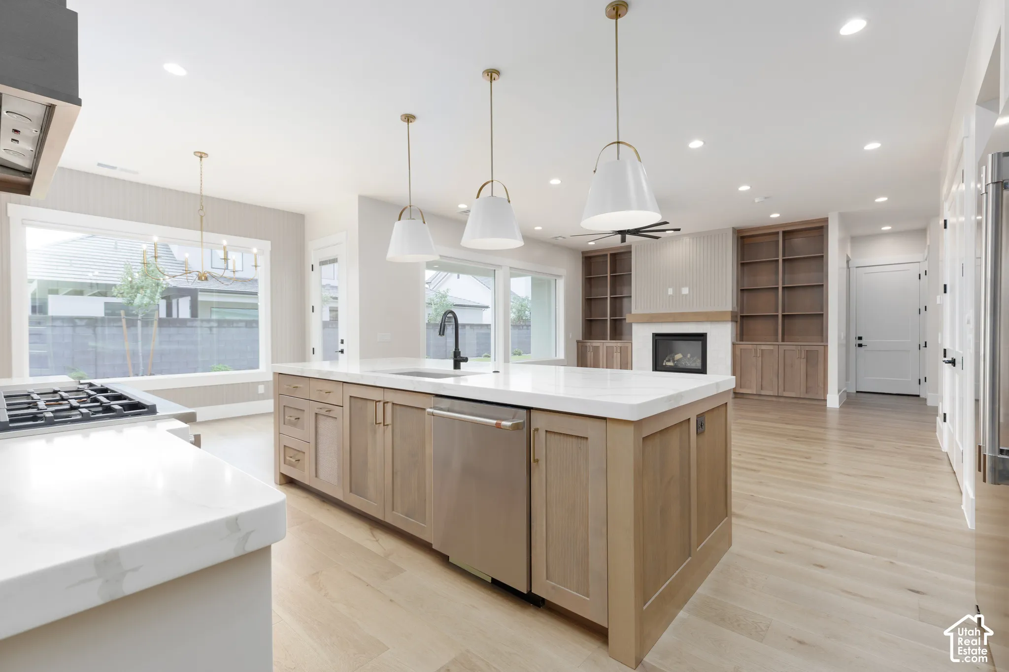 Gourmet kitchen featuring a large central island with light wood cabinetry, stone countertops, integrated stainless steel appliances, and suspended pendant lighting, complemented by built-in wood shelving and wood-finish flooring