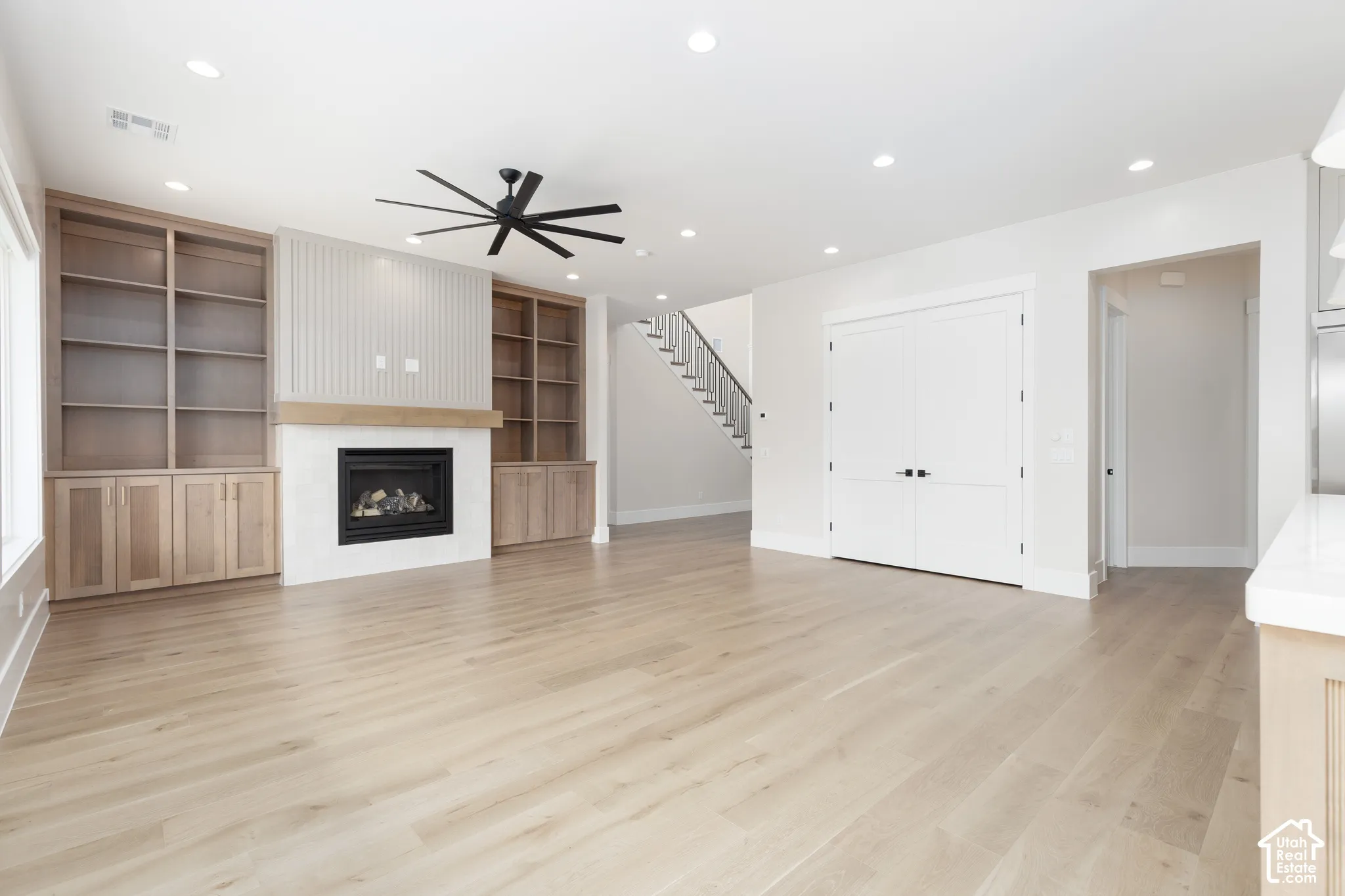 Living area featuring wood-finish flooring, built-in floor-to-ceiling cabinetry, a gas fireplace with a tiled surround, recessed lighting, and a multi-blade ceiling fan
