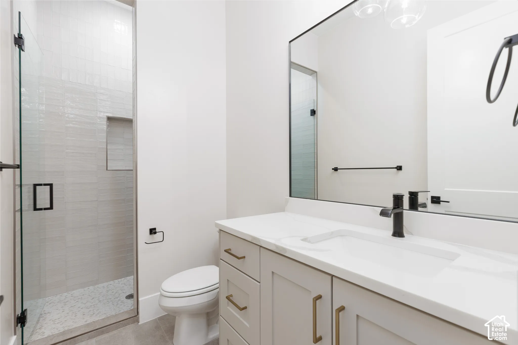 Bathroom featuring a stone-topped vanity with brass-finish hardware, a glass-enclosed shower with tiled walls and an integrated niche, and matte black plumbing fixtures