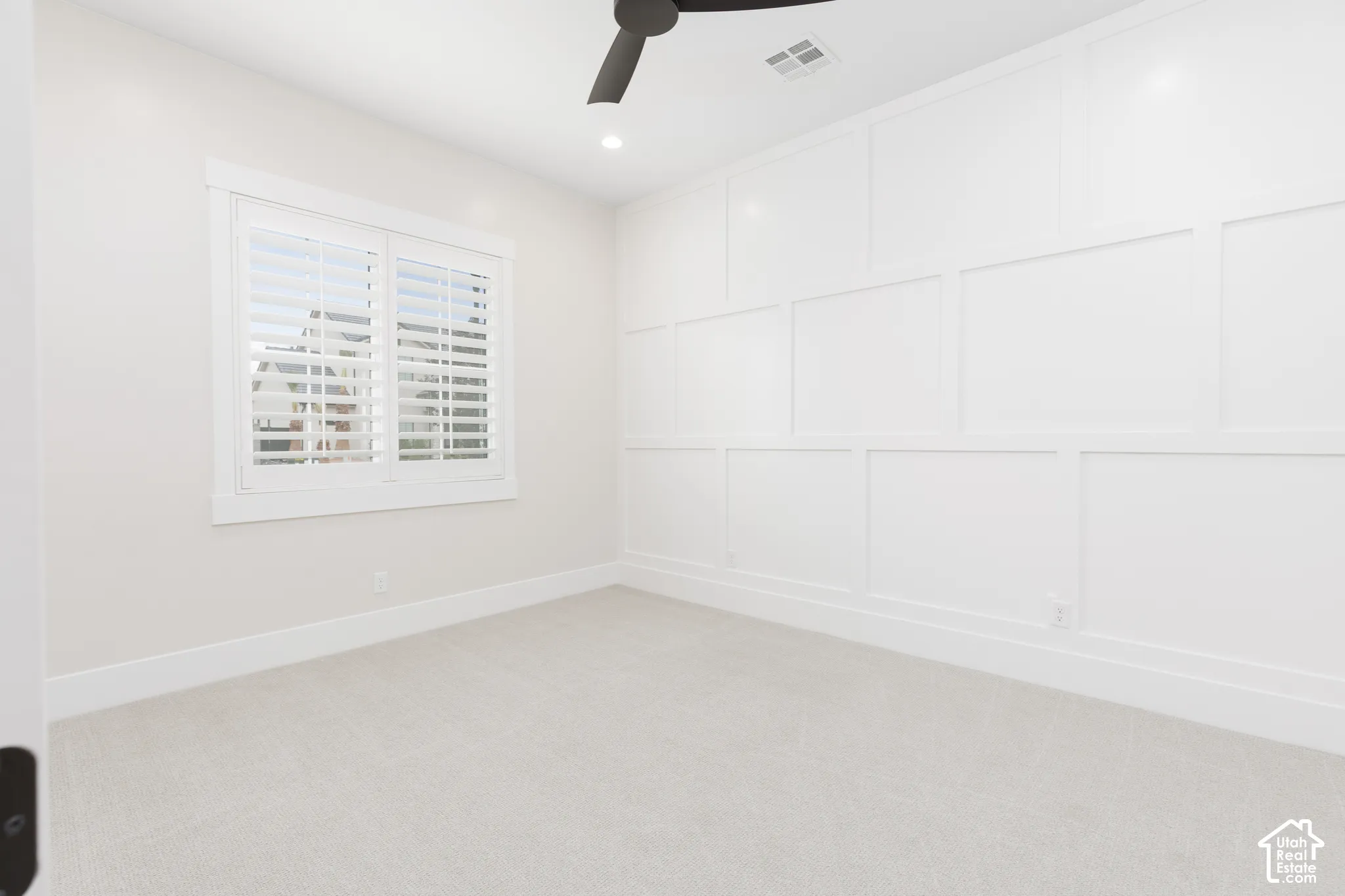 Room featuring crisp board-and-batten wall detailing, white plantation shutters, neutral carpeting, recessed lighting, and a modern ceiling fan