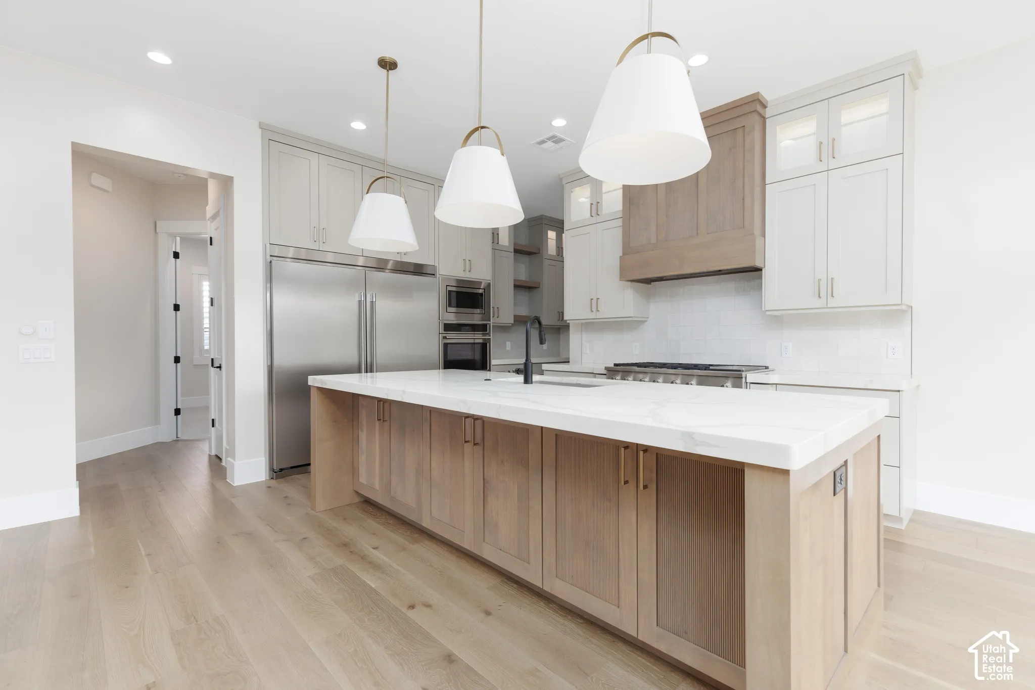 Kitchen featuring custom two-tone cabinetry, expansive stone-surface island, stainless steel refrigerator, professional-grade range with coordinating vent hood, and light wood-finish flooring