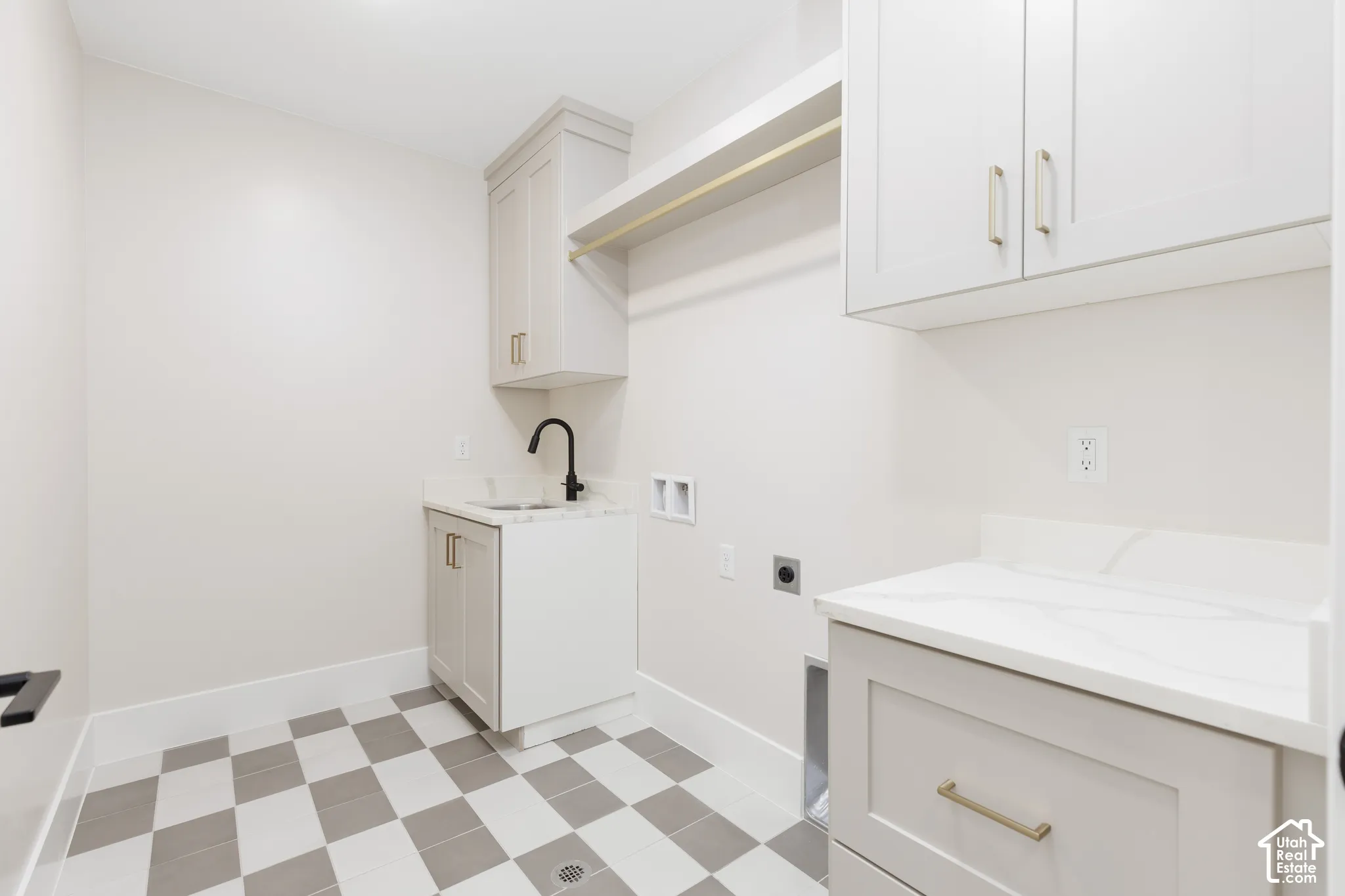 Utility room featuring light-toned cabinetry, stone-finish countertops, matte black faucet, integrated sink, and checkerboard tile flooring