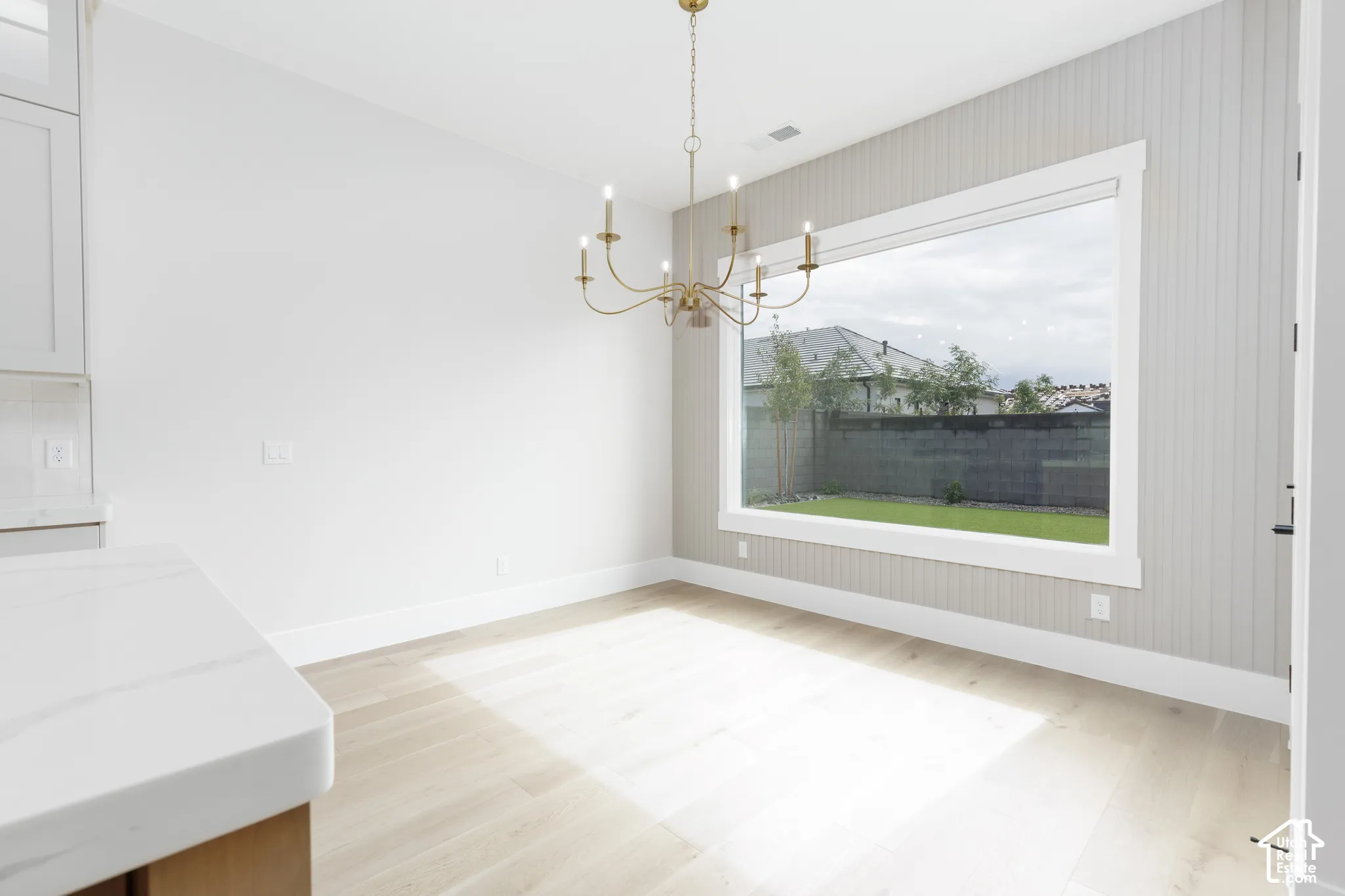 Beadboard accent wall, large picture window, multi-arm metallic chandelier, and light-toned wood-finish flooring