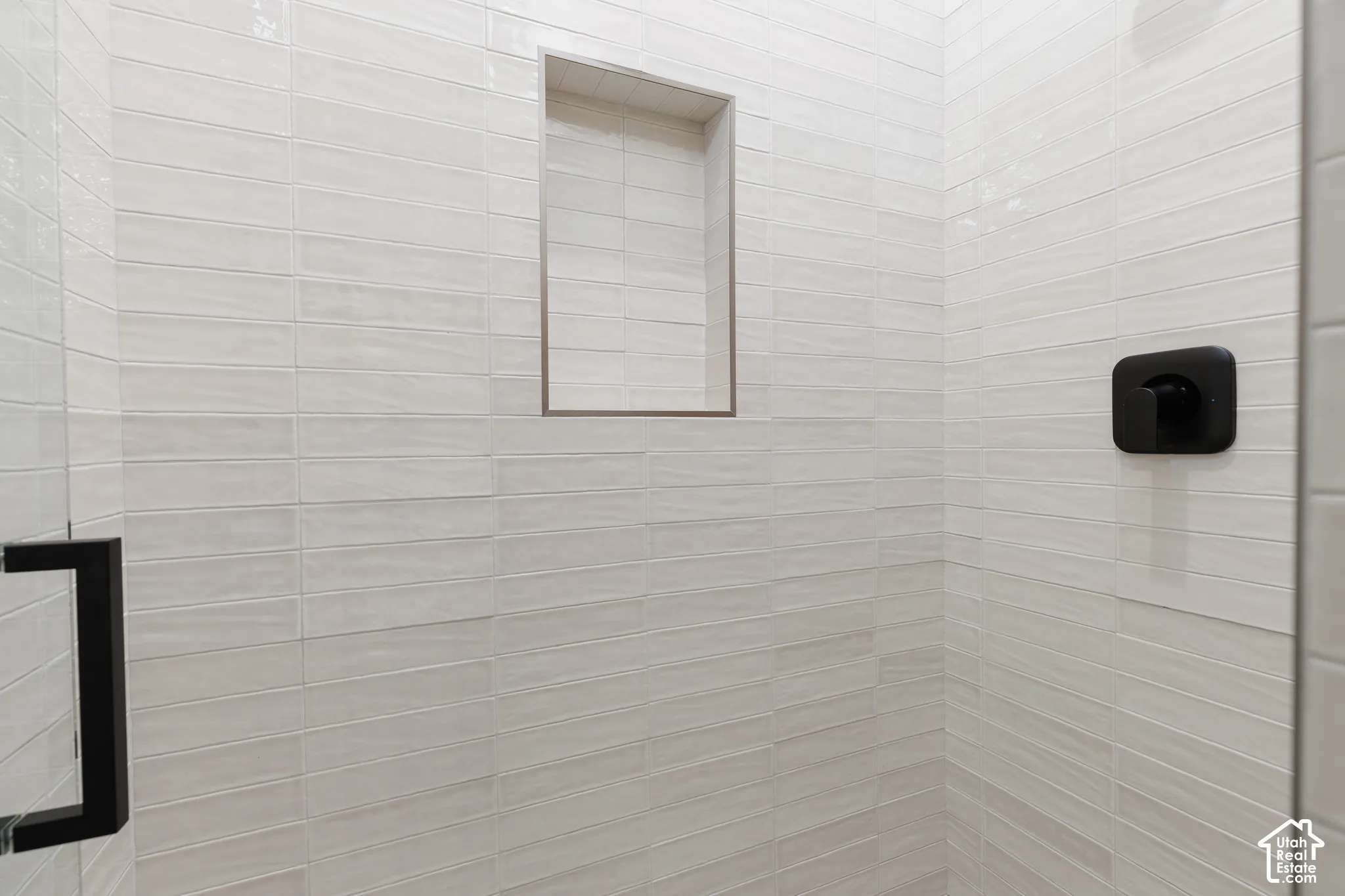 Shower stall featuring light-toned textured subway tile, built-in tiled niche, and matte black hardware