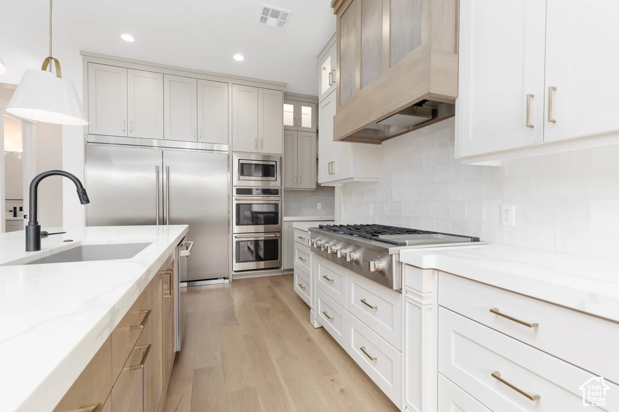 Kitchen featuring custom cabinetry, a built-in stainless steel double oven, a professional-grade gas range, quartz countertops, and wood-finish flooring