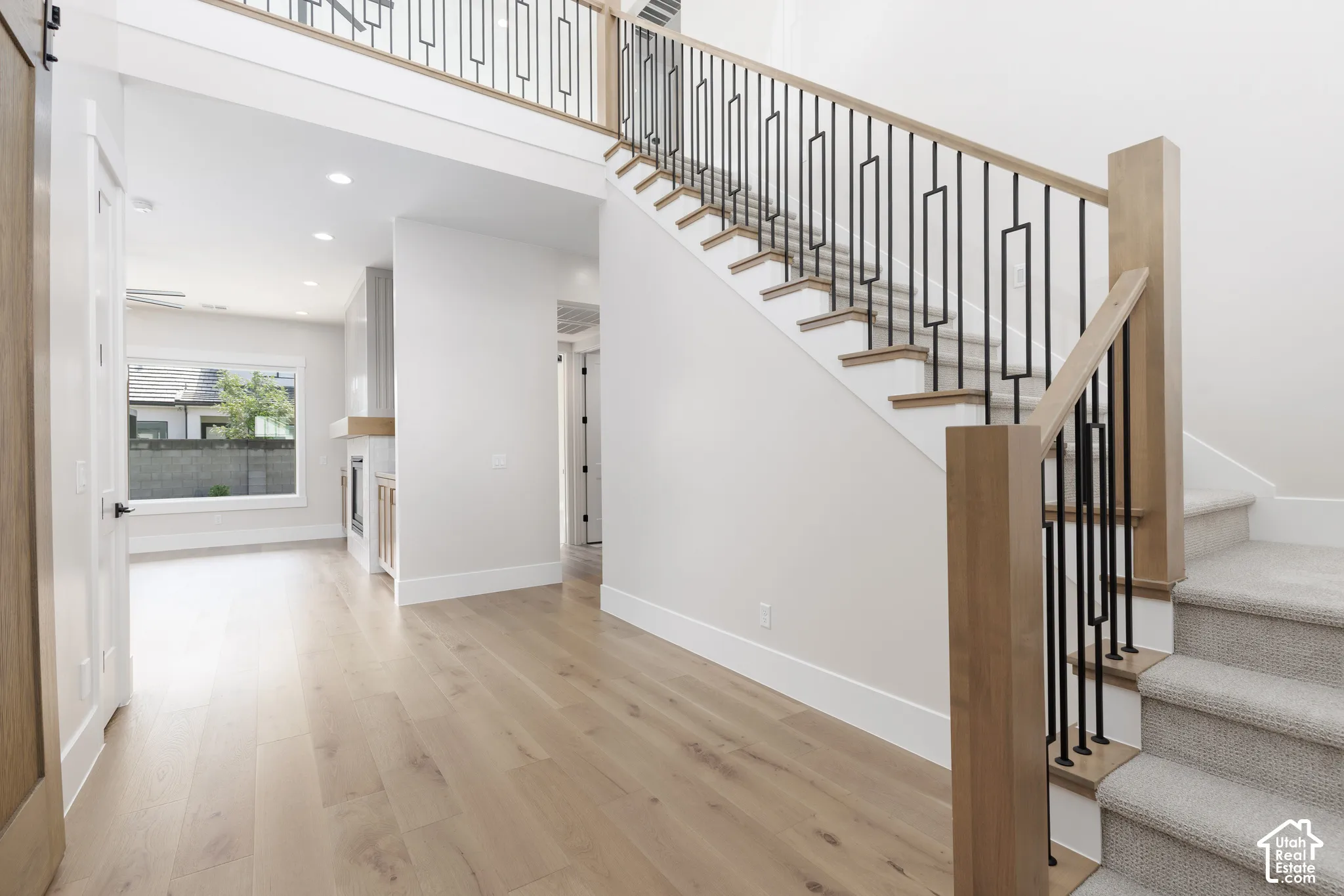 Foyer featuring wood-finish flooring and a staircase with light wood handrails, wood newel posts, and geometric metal balusters