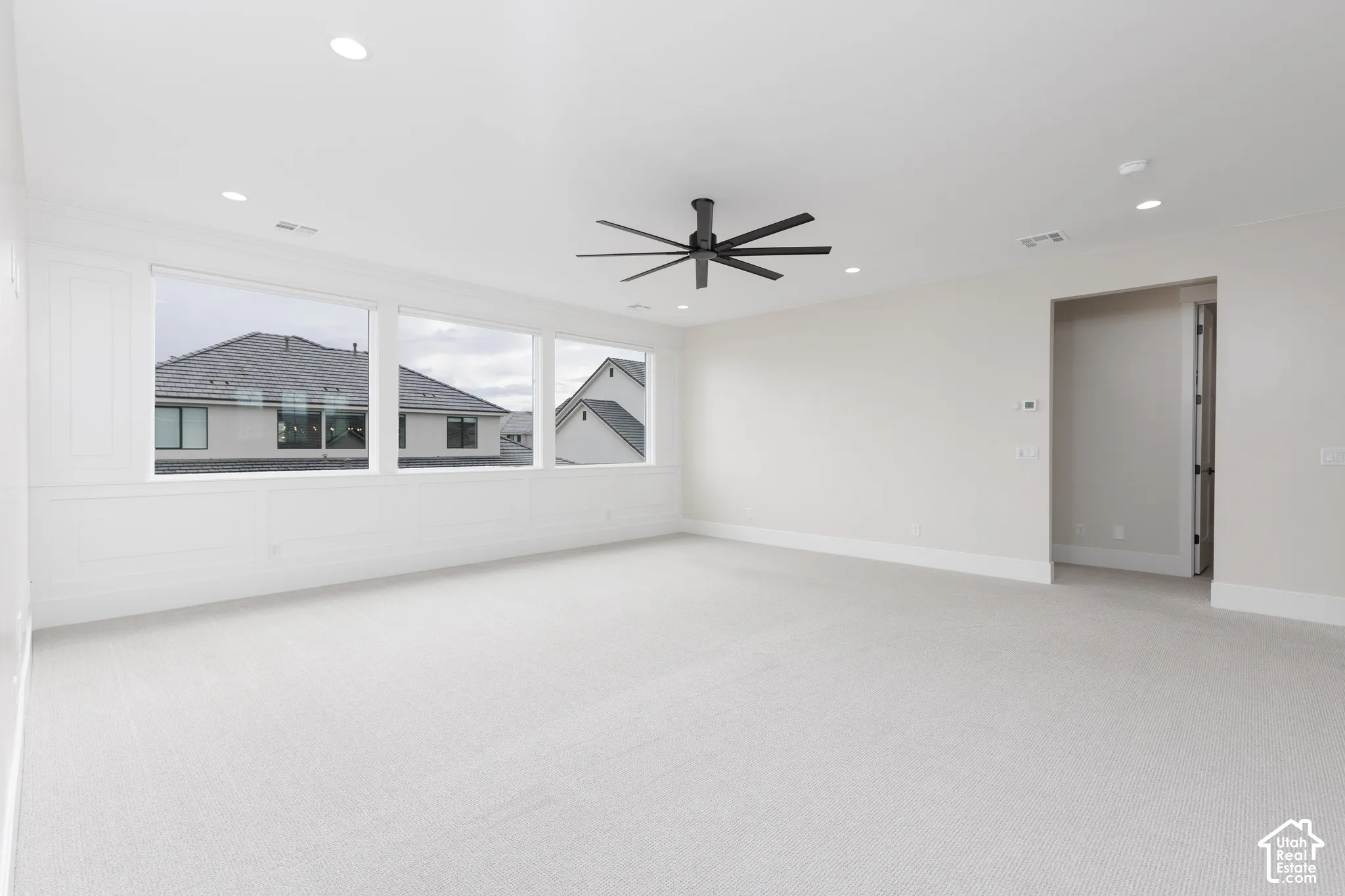 Neutral-toned room featuring expansive windows, recessed lighting, a multi-blade ceiling fan, and decorative wainscoting