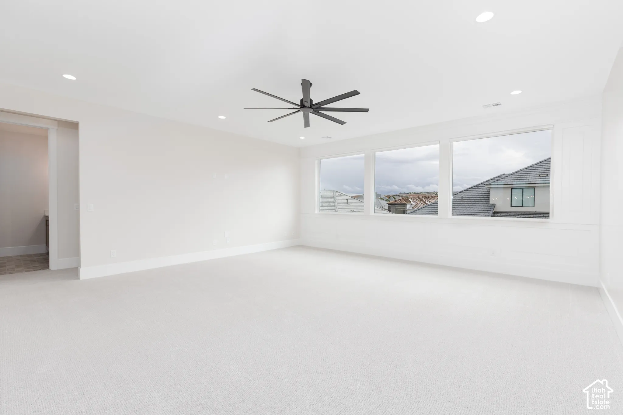 Spacious room featuring neutral carpeting, recessed lighting, a matte black multi-blade ceiling fan, and decorative wainscoting