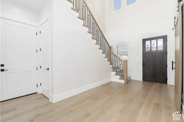 Entryway featuring wood-finish flooring, staircase with metal railings, high ceilings, board-and-batten wall detailing, and a dark-finish door with glass panels
