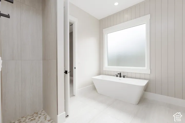 Freestanding white soaking tub with matte black deck-mounted faucet, floor-to-ceiling large-format tile shower surround, vertical board-and-batten wall detailing, and matte black hardware