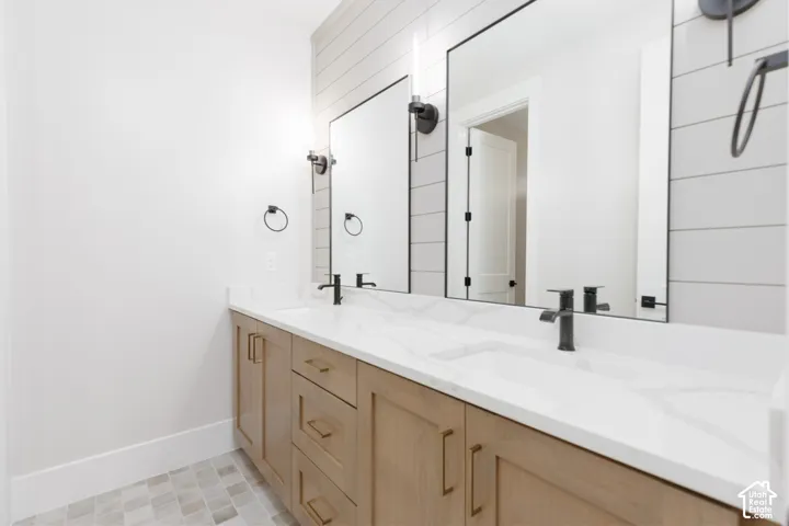 Double vanity featuring a white surface with grey veining, light-toned wood cabinetry, wall-mounted matte black faucets, horizontal shiplap detailing, and rectangular mirrors with black sconces