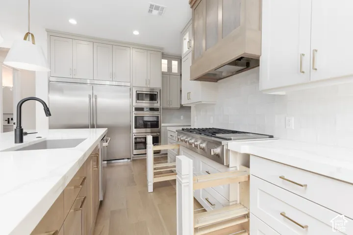 Kitchen featuring custom cabinetry with wood-finish and white shaker-style doors, light-toned stone-surface countertops, professional-grade stainless steel gas range, built-in wall ovens, and matte black faucet fixtures