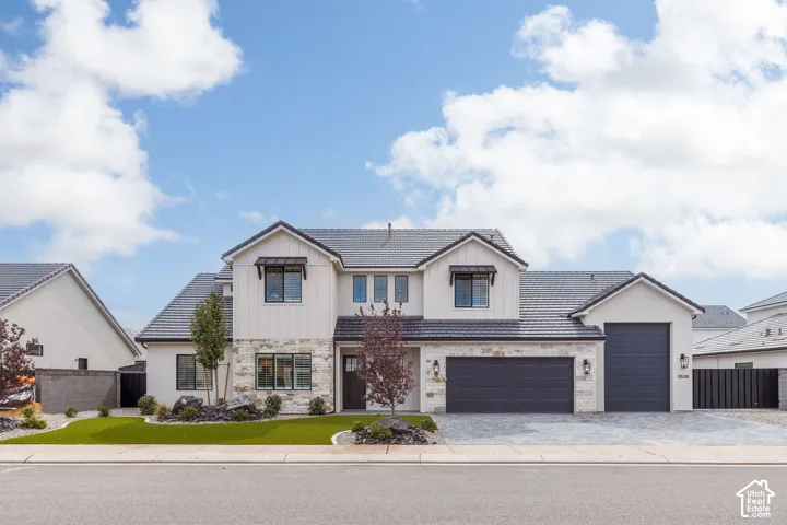 Two-story exterior featuring board-and-batten siding, stone masonry accents, metal window awnings, a tile roof, and a three-car garage