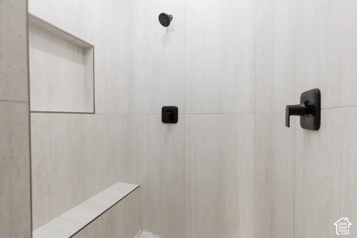 Walk-in shower featuring light-toned large-format tile, matte black fixtures, an integrated wall niche, and a built-in tiled bench