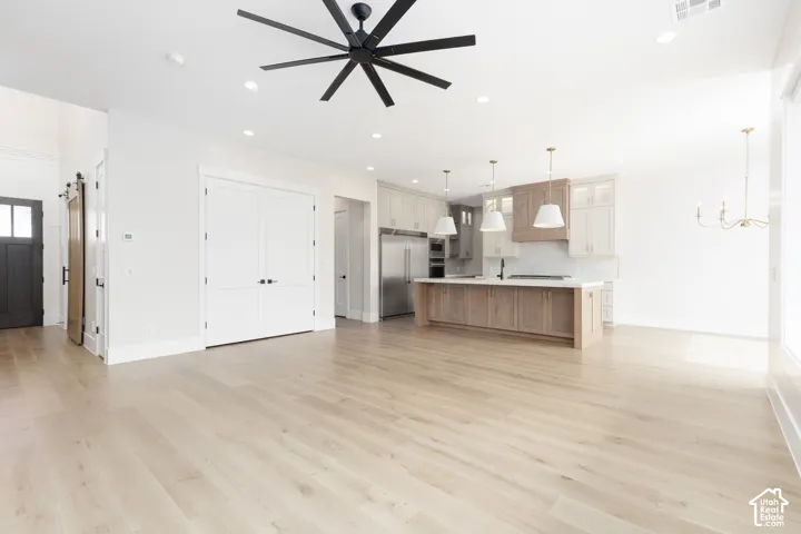 Open-concept interior featuring light wood-finish flooring, a kitchen island with stone countertops, stainless steel appliances, matte black ceiling fan, and recessed lighting