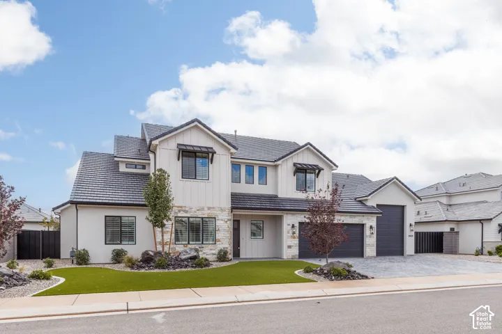 Modern two-story exterior featuring vertical board-and-batten siding, stone masonry accents, a tile roof, and a three-car garage with paver driveway