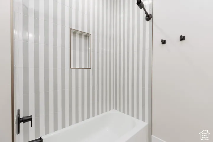 Shower enclosure featuring vertical striped wall tile, built-in recessed wall niche, matte black fixtures, and a white bathtub