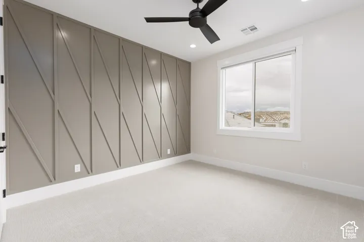 Accent wall with geometric trim detailing, neutral carpeting, sliding window with white casing, and matte black ceiling fan