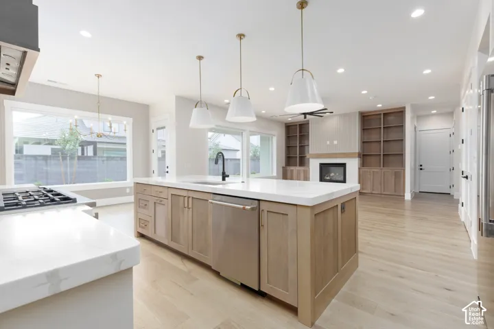 Gourmet kitchen featuring a large central island with light wood cabinetry, stone countertops, integrated stainless steel appliances, and suspended pendant lighting, complemented by built-in wood shelving and wood-finish flooring