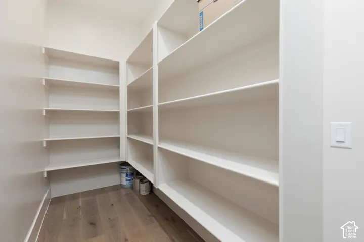 Walk-in storage area featuring custom white built-in shelving and wood-finish flooring