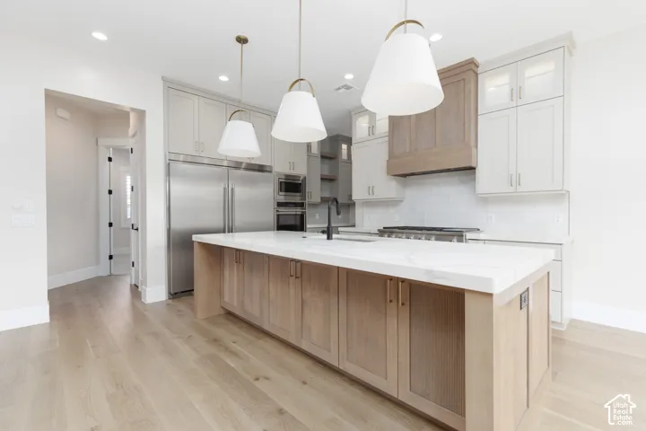 Kitchen featuring custom two-tone cabinetry, expansive stone-surface island, stainless steel refrigerator, professional-grade range with coordinating vent hood, and light wood-finish flooring