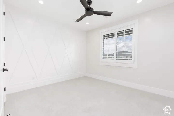 Room featuring an accent wall with geometric millwork, neutral carpeting, a matte black ceiling fan, and window shutters