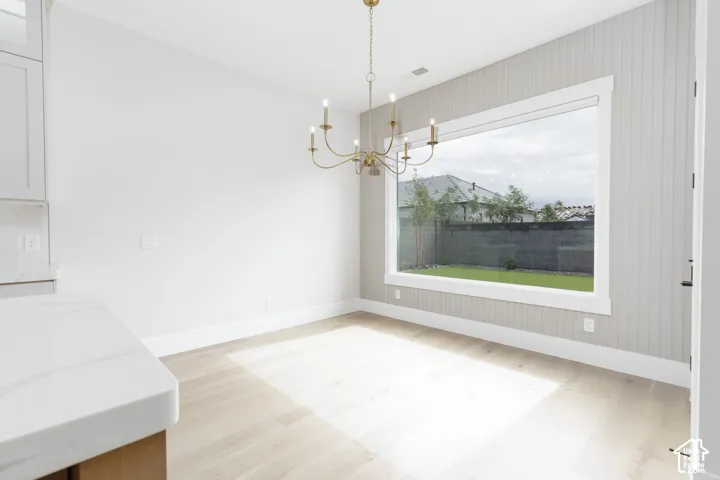 Beadboard accent wall, large picture window, multi-arm metallic chandelier, and light-toned wood-finish flooring