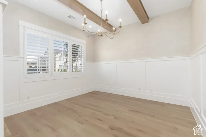 Interior space featuring wood-finish flooring, white wall wainscoting, a multi-arm metallic chandelier, ceiling wood-tone beams, and windows with interior shutters