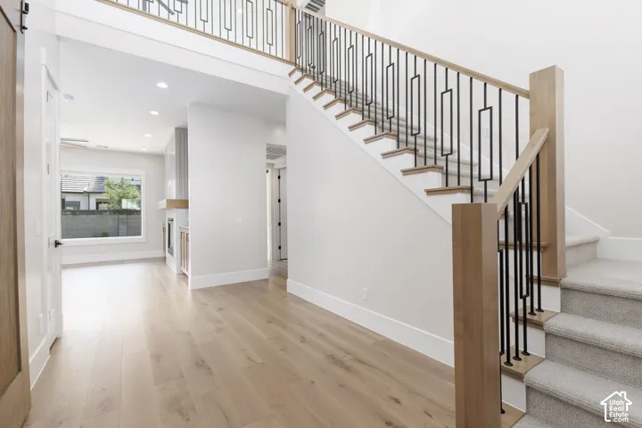 Foyer featuring wood-finish flooring and a staircase with light wood handrails, wood newel posts, and geometric metal balusters