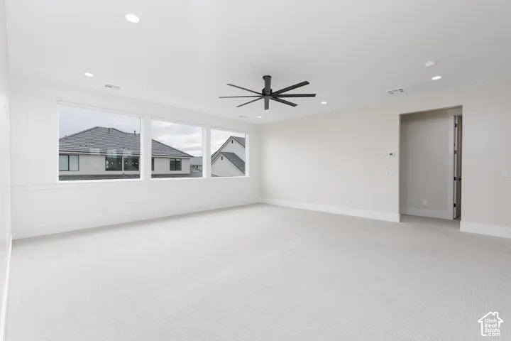Neutral-toned room featuring expansive windows, recessed lighting, a multi-blade ceiling fan, and decorative wainscoting