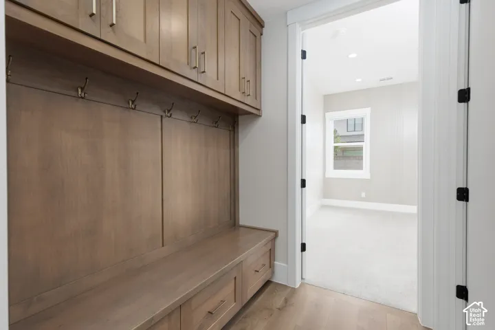 Built-in wood-finish cabinetry featuring overhead storage, metal coat hooks, and integrated bench seating with lower drawer storage, paired with wood-finish flooring