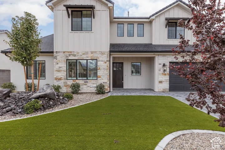 Contemporary two-story exterior featuring vertical board-and-batten siding, stacked stone masonry, a dark-toned tile roof, and a paved stone driveway