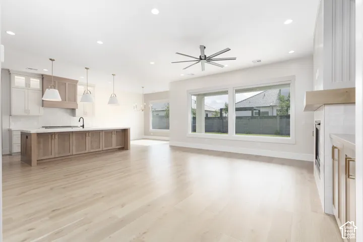 Open-concept interior featuring light wood-finish flooring, recessed lighting, a multi-blade ceiling fan, expansive windows, and a kitchen island with built-in cabinetry