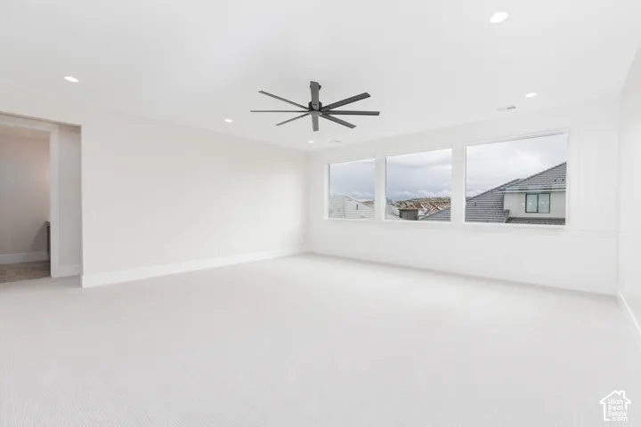 Spacious room featuring neutral carpeting, recessed lighting, a matte black multi-blade ceiling fan, and decorative wainscoting
