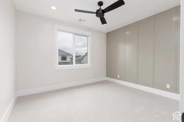 Neutral-toned room featuring a decorative board-and-batten accent wall, neutral carpeting, recessed ceiling lighting, and a matte black ceiling fan