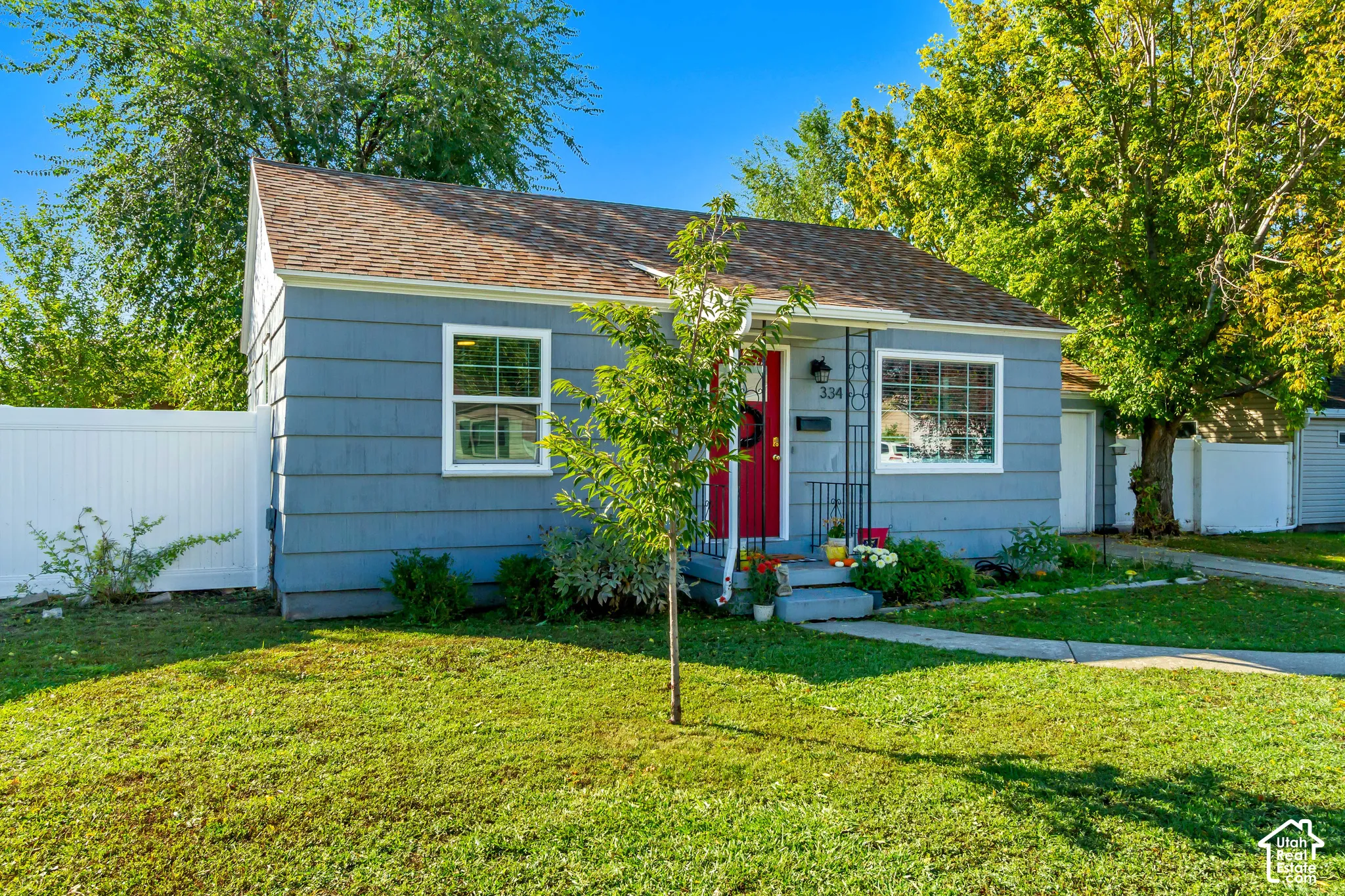 Exterior featuring blue lap siding, an asphalt shingle roof, a red front door, white vinyl fencing, and a concrete walkway