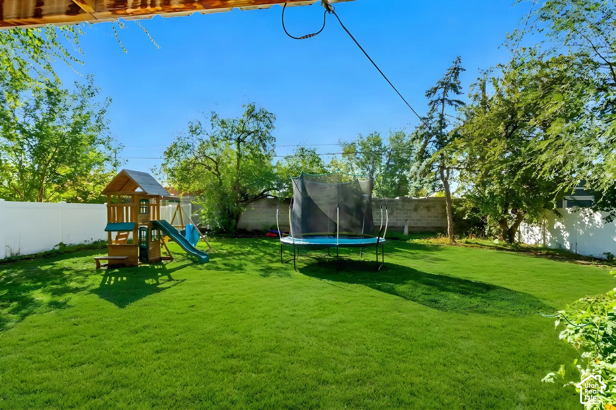 Expansive backyard featuring a level lawn, mature trees, and a white privacy fence