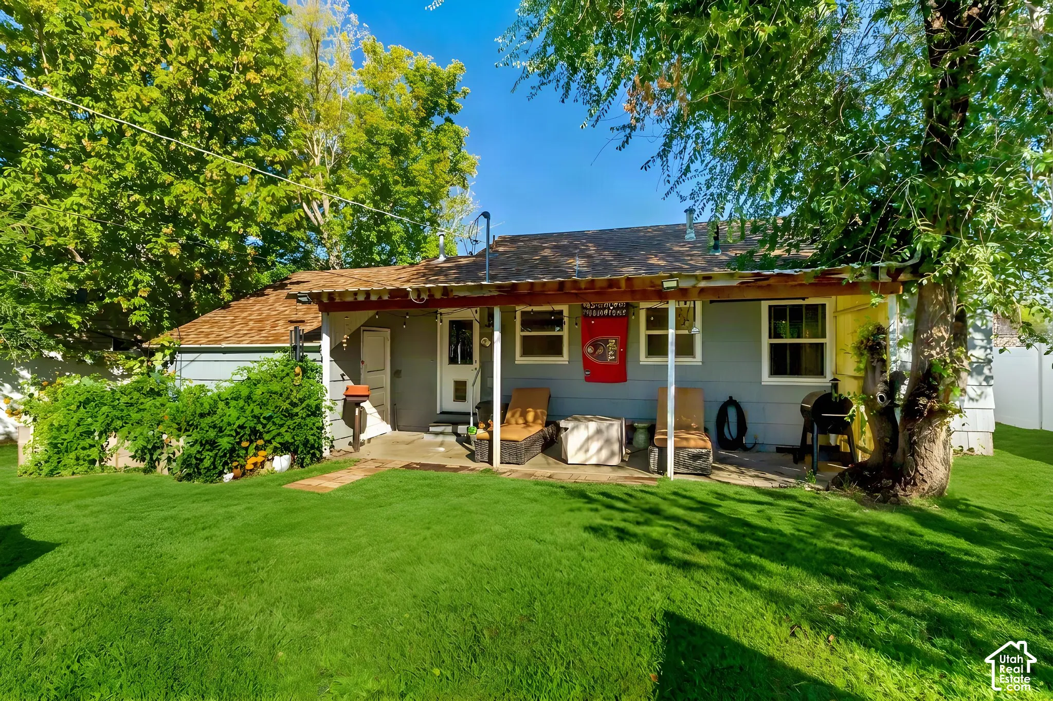 Backyard featuring a concrete patio, a covered porch, mature trees, and a grass lawn
