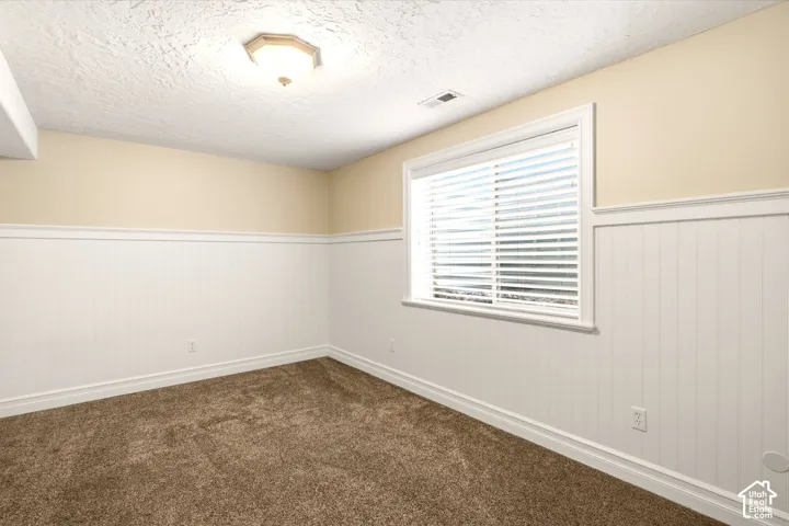 Room featuring neutral carpeting, white wainscoting, textured ceiling, and a multi-pane sliding window