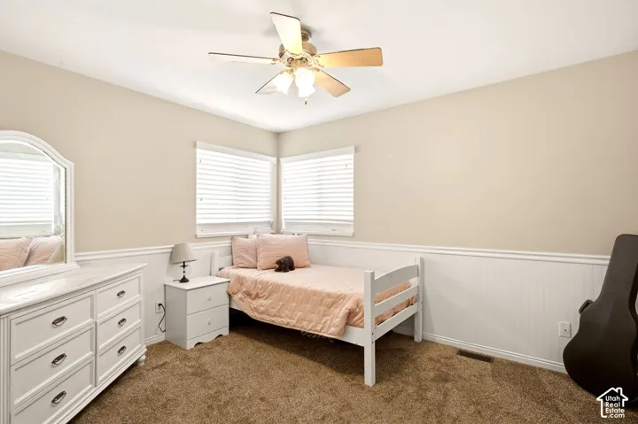Neutral interior featuring white wainscoting, dual corner windows with horizontal blinds, carpeting, and a central ceiling fan with multi-light fixture