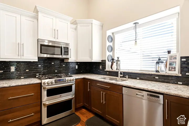 Kitchen featuring white upper cabinetry, dark wood lower cabinetry, stone-finish countertops, stainless steel appliances, and a black tile backsplash