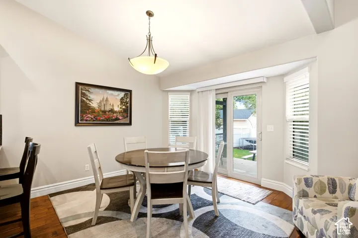 Dining area featuring wood-finish flooring, a vaulted ceiling, a pendant light fixture, a bay window with blinds, and glass sliding doors