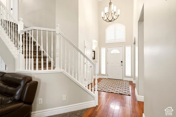 Grand foyer featuring double-height ceilings, wood-finish flooring, a white staircase with a traditional balustrade, an arched transom window, and a multi-arm chandelier