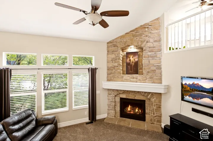 Full-height natural stone fireplace featuring a mantle and integrated display niche, complemented by vaulted ceilings, a ceiling fan, and large windows