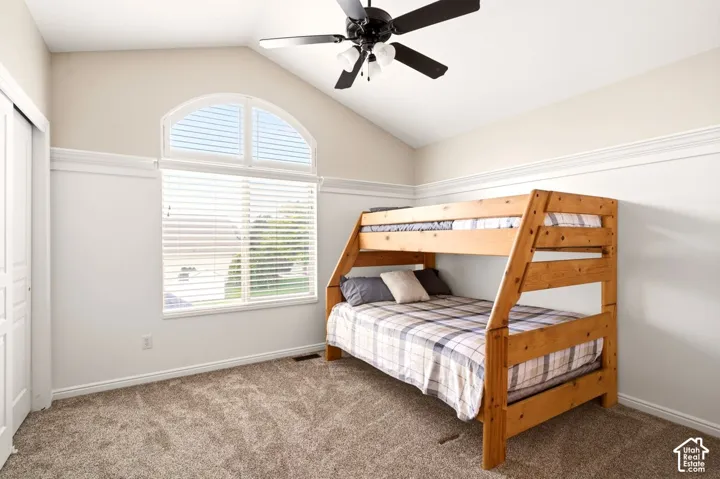 Vaulted ceiling featuring an arched window, decorative chair rail molding, wall-to-wall carpeting, and a multi-blade ceiling fan with integrated lighting