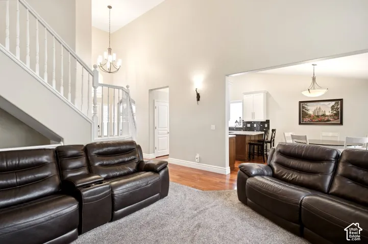 High-volume ceilings featuring a multi-tier chandelier, staircase with white balusters, wood-finish flooring, and pendant lighting