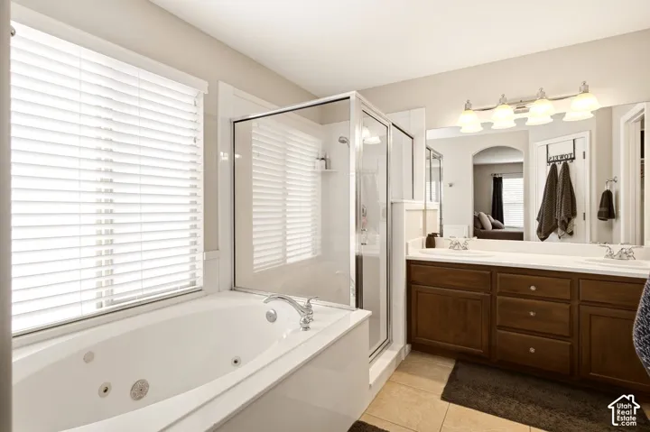 Jetted soaking tub, glass-enclosed shower, dual-sink vanity with wood cabinetry, and large-format wall mirror with overhead lighting