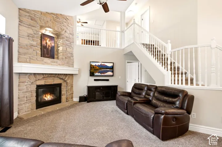 Vaulted ceilings, full-height stone fireplace with a prominent hearth, staircase with white balusters, and a carpeted mezzanine overlook