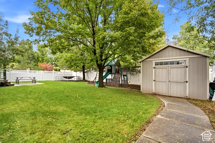 Fenced backyard featuring a manicured lawn, detached storage shed, concrete pathway, and mature trees